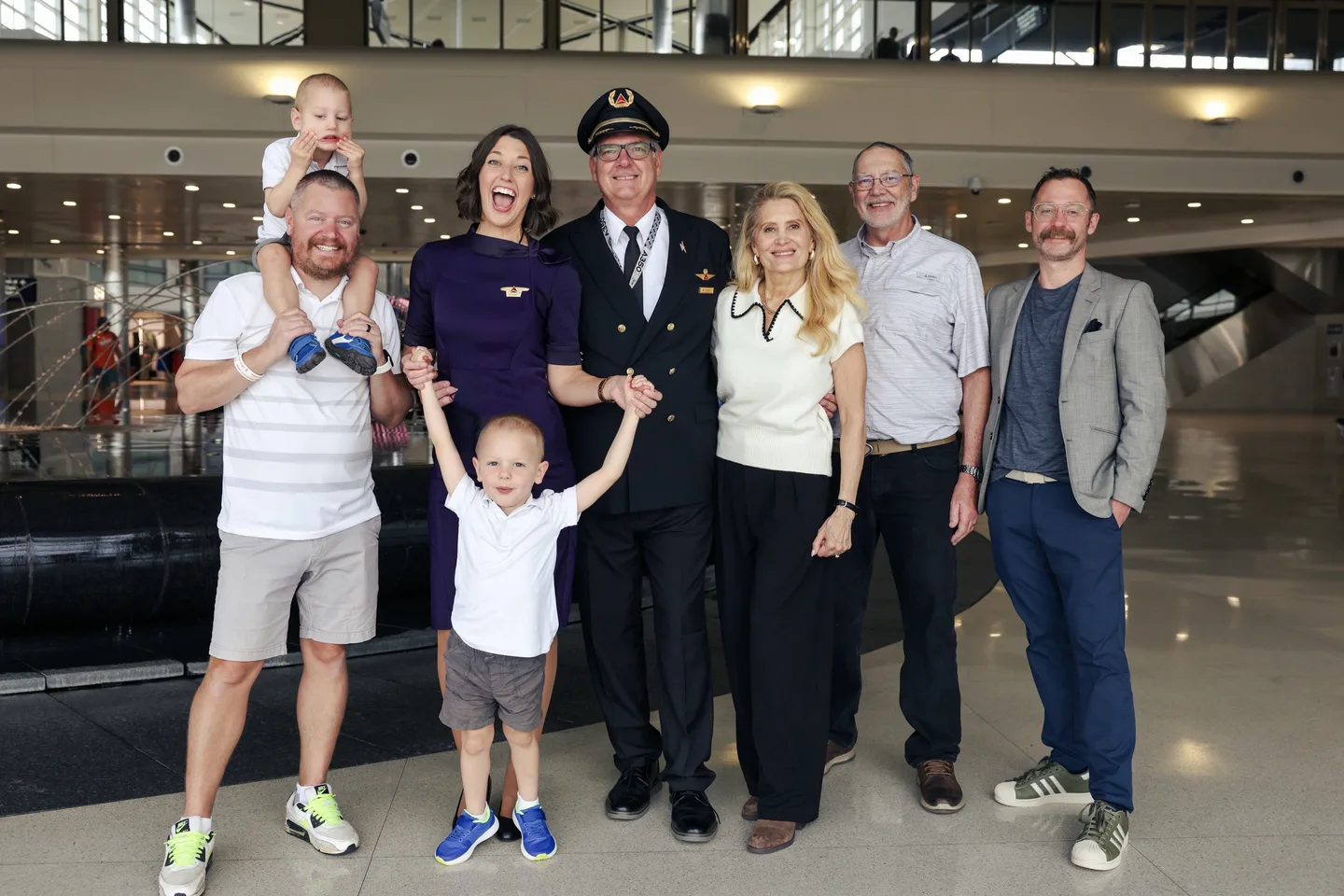 A group smiling with children and an airline pilot in an airport terminal